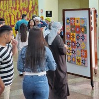 Público observa quadro com mosaico de estrelas coloridas e painel de rostos ao fundo no Espaço Cultural Célia Câmara