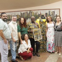 Grupo de artistas e corpo servidor posam junto a quadro e manequim com vestimenta de estampa africana