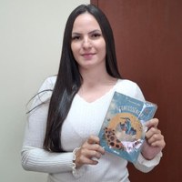 Mulher jovem segurando livro intitulado Acontessências em frente a porta de madeira