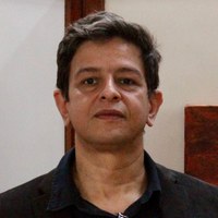 Retrato de rosto de homem com cabelos castanhos e camisa preta em ambiente de exposição