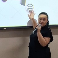 Rose Borges aponta para slide com ícone de face sorridente durante tópico sobre saúde mental e relações interpessoais no trabalho