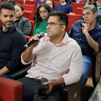 Homem sentado em poltrona vermelha de auditório fazendo pergunta com microfone durante evento de atualização jurídica