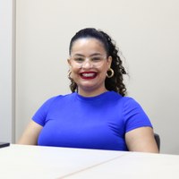 Servidora da Escola Legislativa, sorridente com blusa azul e óculos participa de programação especial do Mês da Mulher na CMG