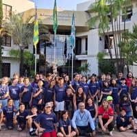 Crianças de uniforme azul da escola Athletics sentadas em praça externa da Câmara