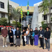 Grupo de pessoas adultas em visita técnica posam em frente a chafariz e bandeiras