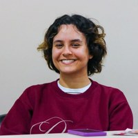 Retrato de jovem sorridente, integrante de grupo visitante, sentada em mesa de reunião