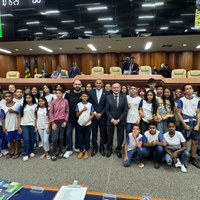 Visão ampla do plenário com vereança e estudantes posicionados à frente da mesa diretora para fotografia oficial