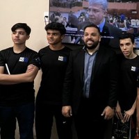 Estudantes de camiseta preta posam com Vereador Gerverson Abel em frente a monitor de TV