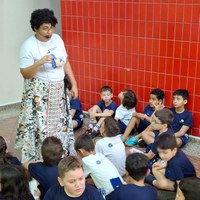 Servidora da Câmara Municipal de Goiânia conduz atividade de educação para cidadania com grupo de crianças sentadas no chão